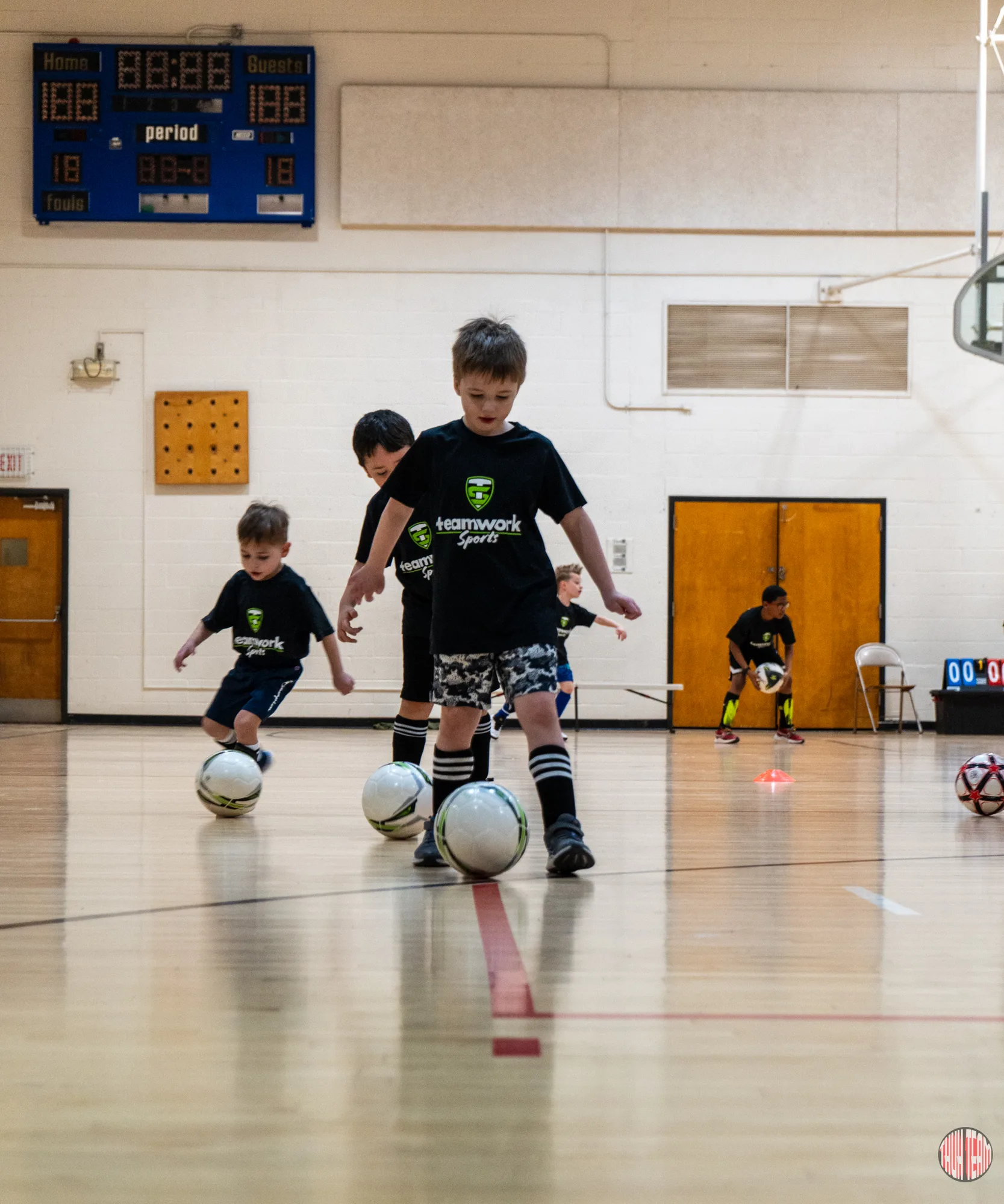 Young players dribbling soccer balls through a drill in a gym