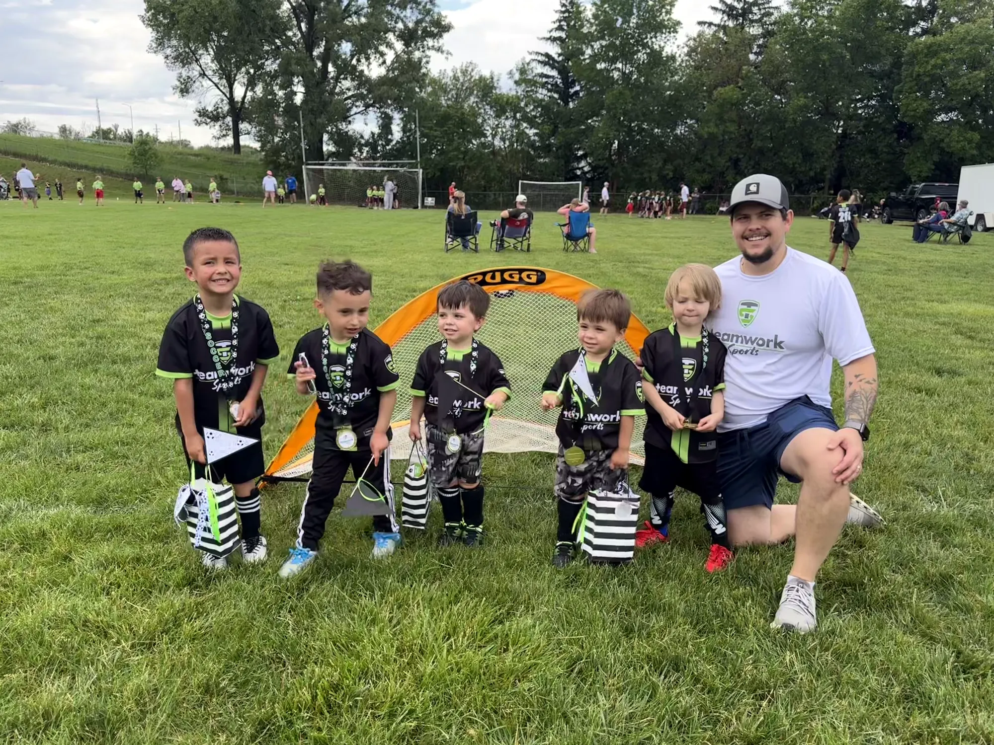 Young soccer players in Teamwork jerseys showing off their medals with their coach